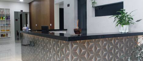 A reception desk with a geometric patterned design, a potted plant, and a modern interior with a wooden accent wall and pendant lighting.