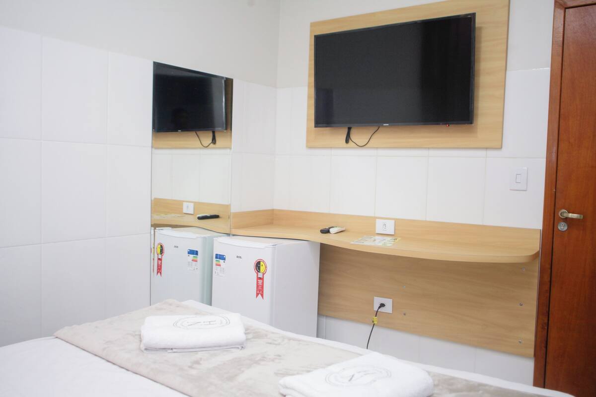 Una camera d'albergo con un letto, un piccolo frigorifero, un bancone in legno e un televisore montato a parete.