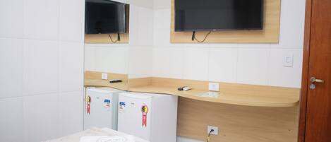 Habitación de hotel con cama, refrigerador pequeño, mostrador de madera y televisión montada en la pared.