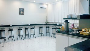Cozinha moderna com armários brancos, bancada preta e banquetas.