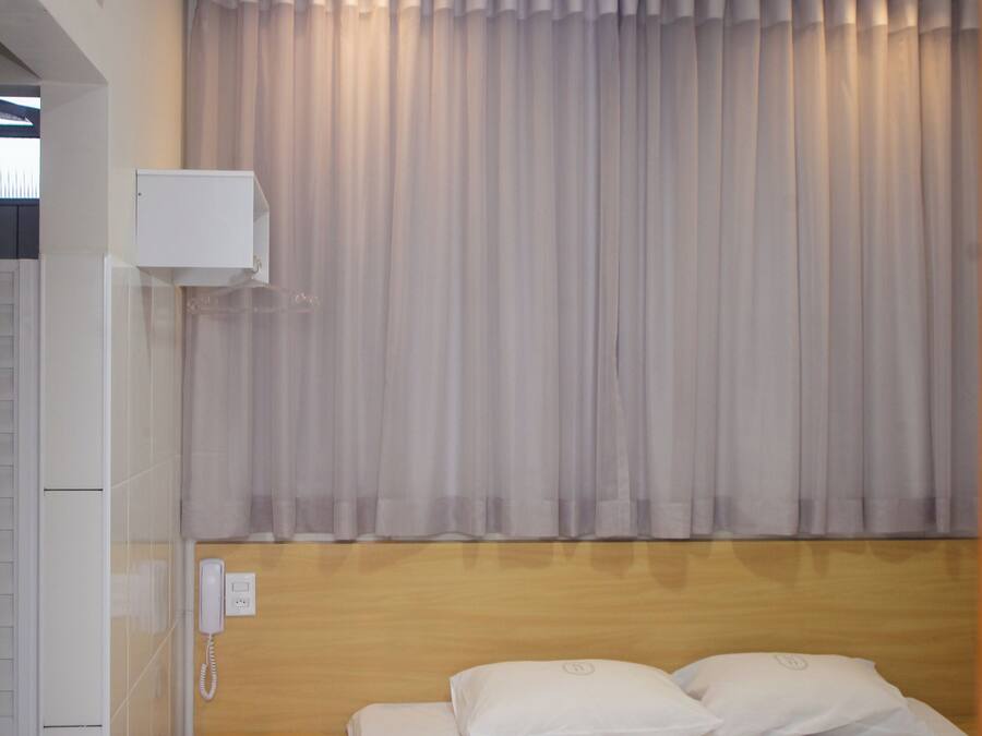 Una habitación de hotel con una cama, cabecera de madera, unidad de aire acondicionado blanca y cortina.