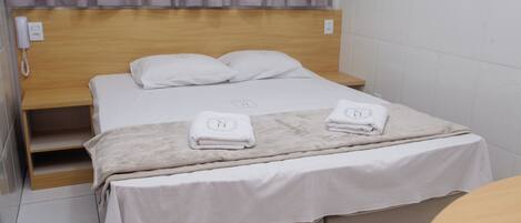 Ein Hotelzimmer mit einem hölzernen Kopfteil, einem Bett mit weißen Bettwäsche, zwei Handtüchern auf dem Bett, einem Nachttisch und einem Telefon an der Wand.