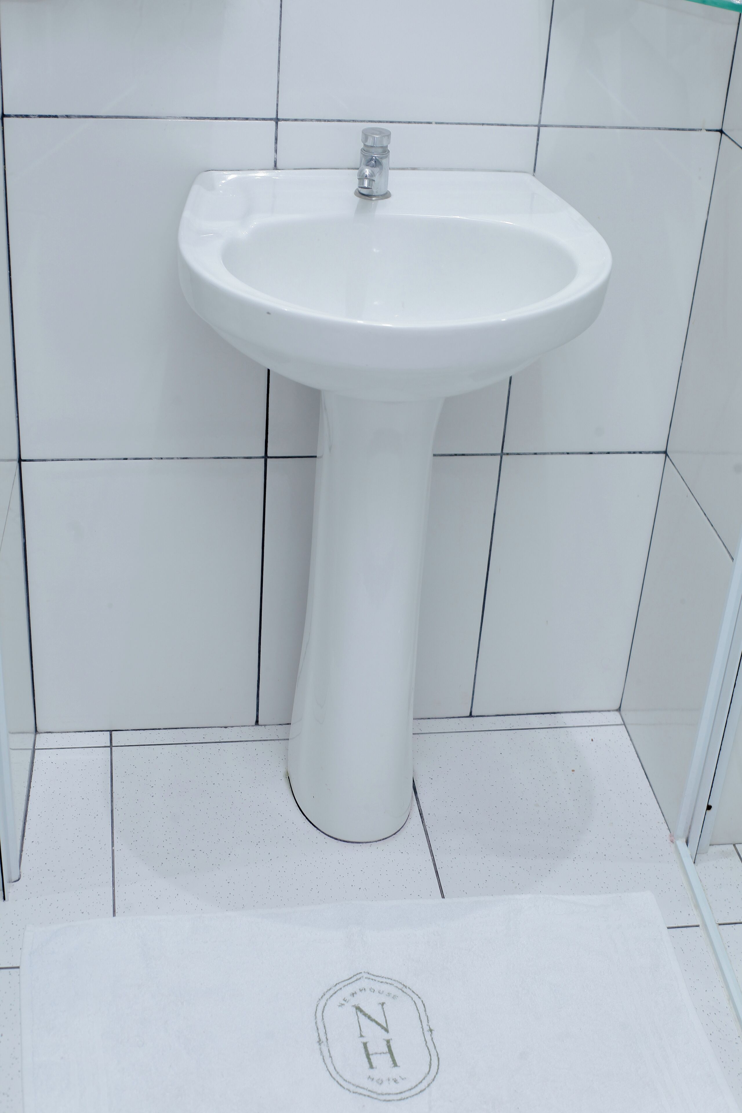 A white bathroom with a pedestal sink and white tiled walls.