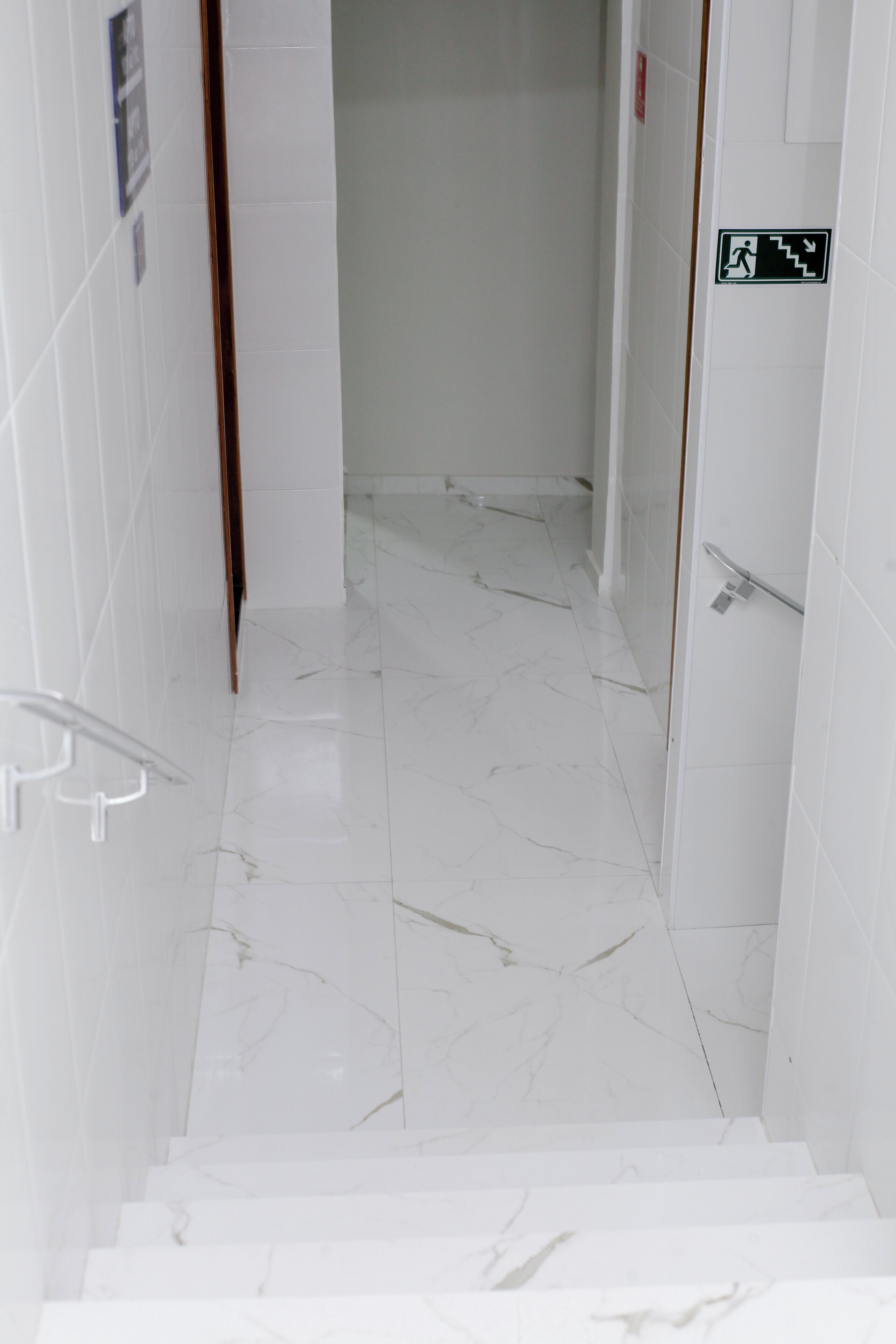 A clean, white-tiled staircase leading to a room with a door marked by an emergency exit sign.