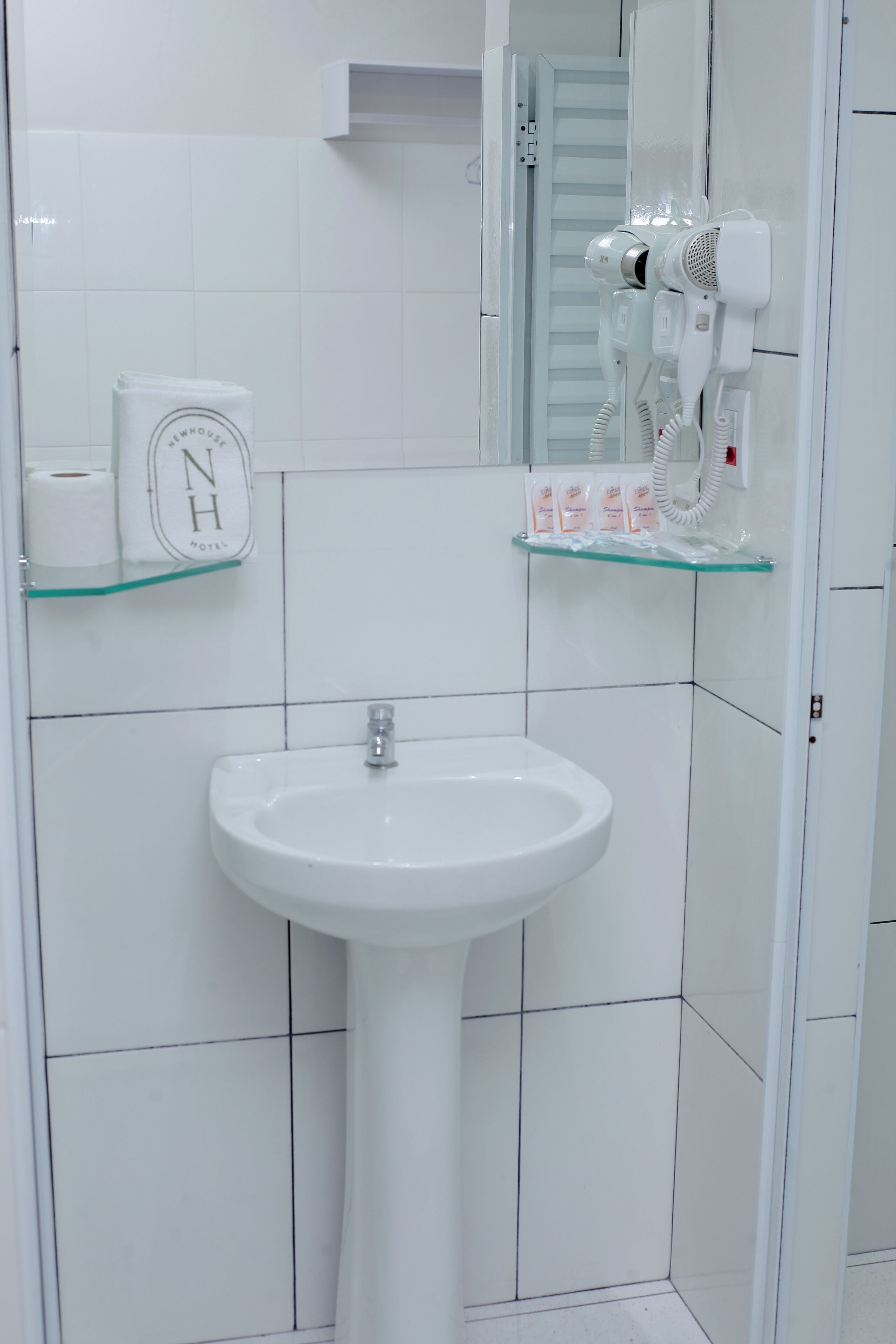 A bathroom with a white sink, a hairdryer, and toiletries on a glass shelf.