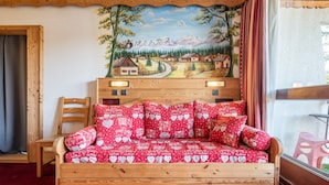 Una cama de madera con colcha y almohadas estampadas en rojo, un cabecero de madera y un mural de un pueblo de montaña en la pared.