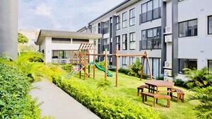Un edificio moderno con un parque infantil, que incluye toboganes y columpios, y una mesa de picnic.