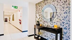 Un pasillo moderno con un papel tapiz de diseño geométrico, un espejo redondo y una consola decorada con objetos ornamentales.