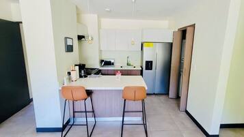 Una cuina compacta amb una illa central, dos tamborets d'abarca i un refrigerador i microones.