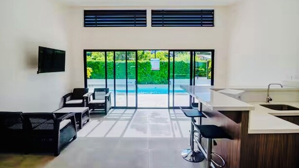 Una cocina moderna con una isla grande, un comedor con taburetes de bar y vistas a una piscina.