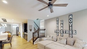 Una sala de estar moderna con un sofá modular, un ventilador de techo y una pared con la inscripción 'MOVIE TOGETHER'.