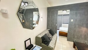 A modern bedroom with a geometric mirror, a bed with patterned bedding, a small desk with a tablet, and a potted plant.
