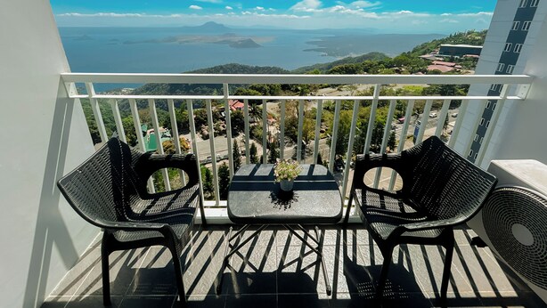 A balcony with two chairs and a table, overlooking a coastal landscape with mountains and a body of water.