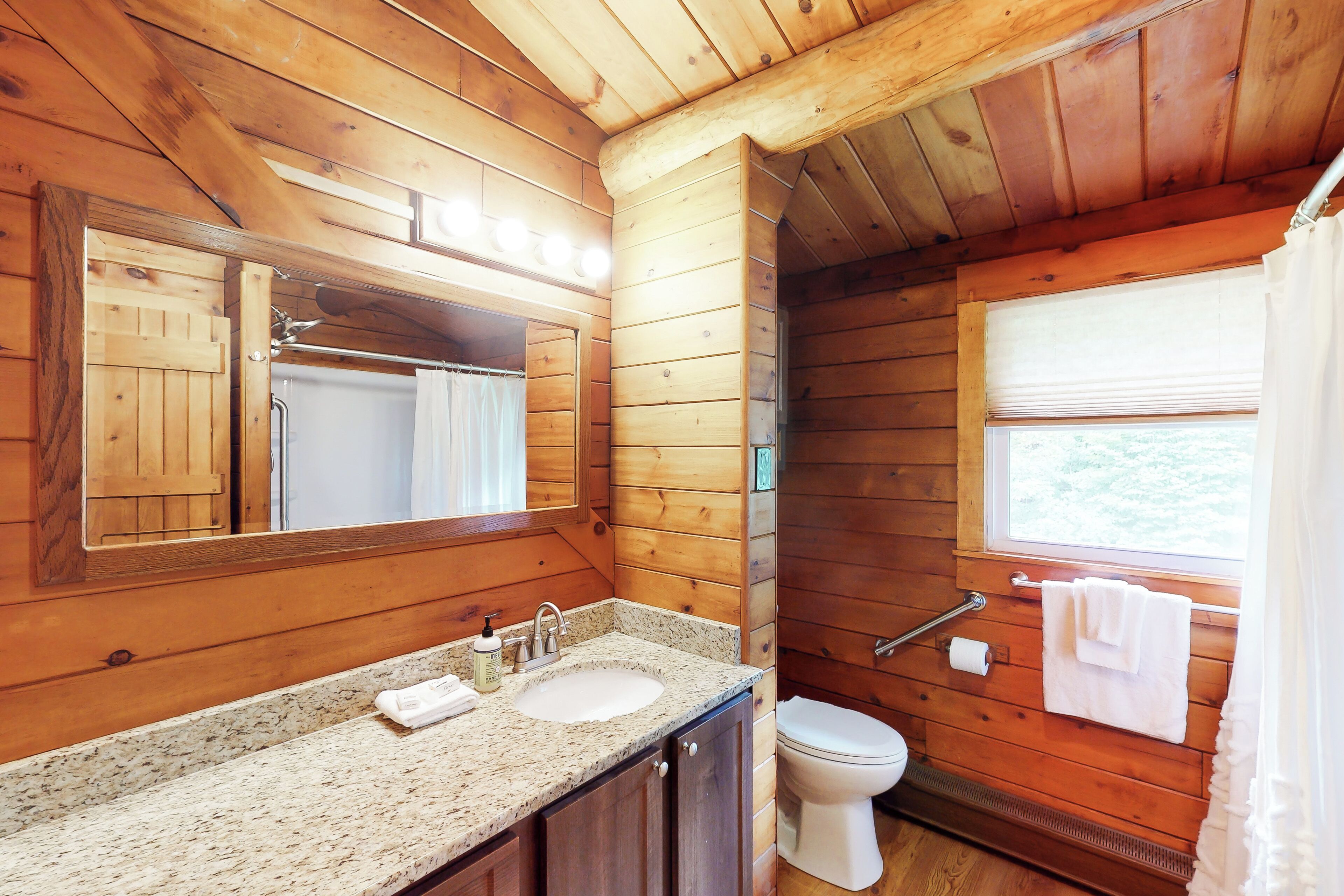 Ein Badezimmer einer Holzhütte mit Waschbecken, Spiegel und Toilette.