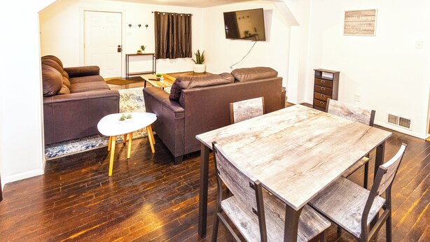 Un espacio habitable compacto con un sofá, una mesa de comedor y un televisor montado en la pared.