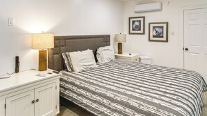 Quarto com cama, luminárias de cabeceira, mesa de cabeceira, cômoda e ar condicionado na parede.