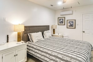 A bedroom with a bed, bedside lamps, a nightstand, a dresser, and an air conditioning unit on the wall.