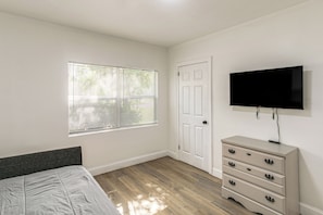 Un dormitorio con cama, cómoda, televisor y ventana con persianas.