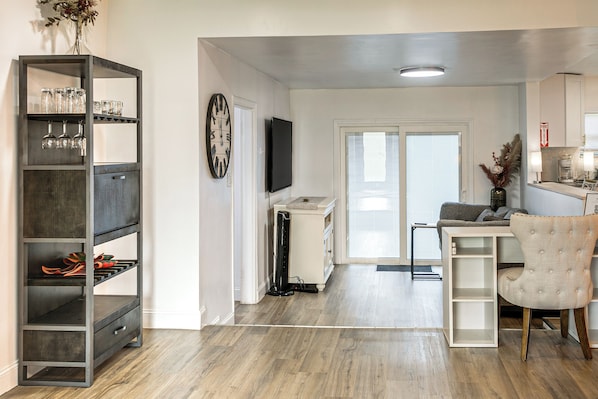 A modern living room with a wooden floor, a grey shelving unit, a flat-screen TV, and a grey sofa.