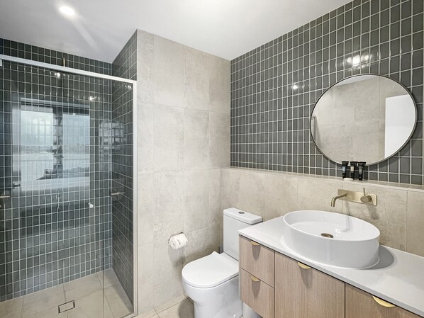 Une salle de bain moderne avec une douche à parois de verre, des toilettes et un lavabo surmonté d’un miroir.