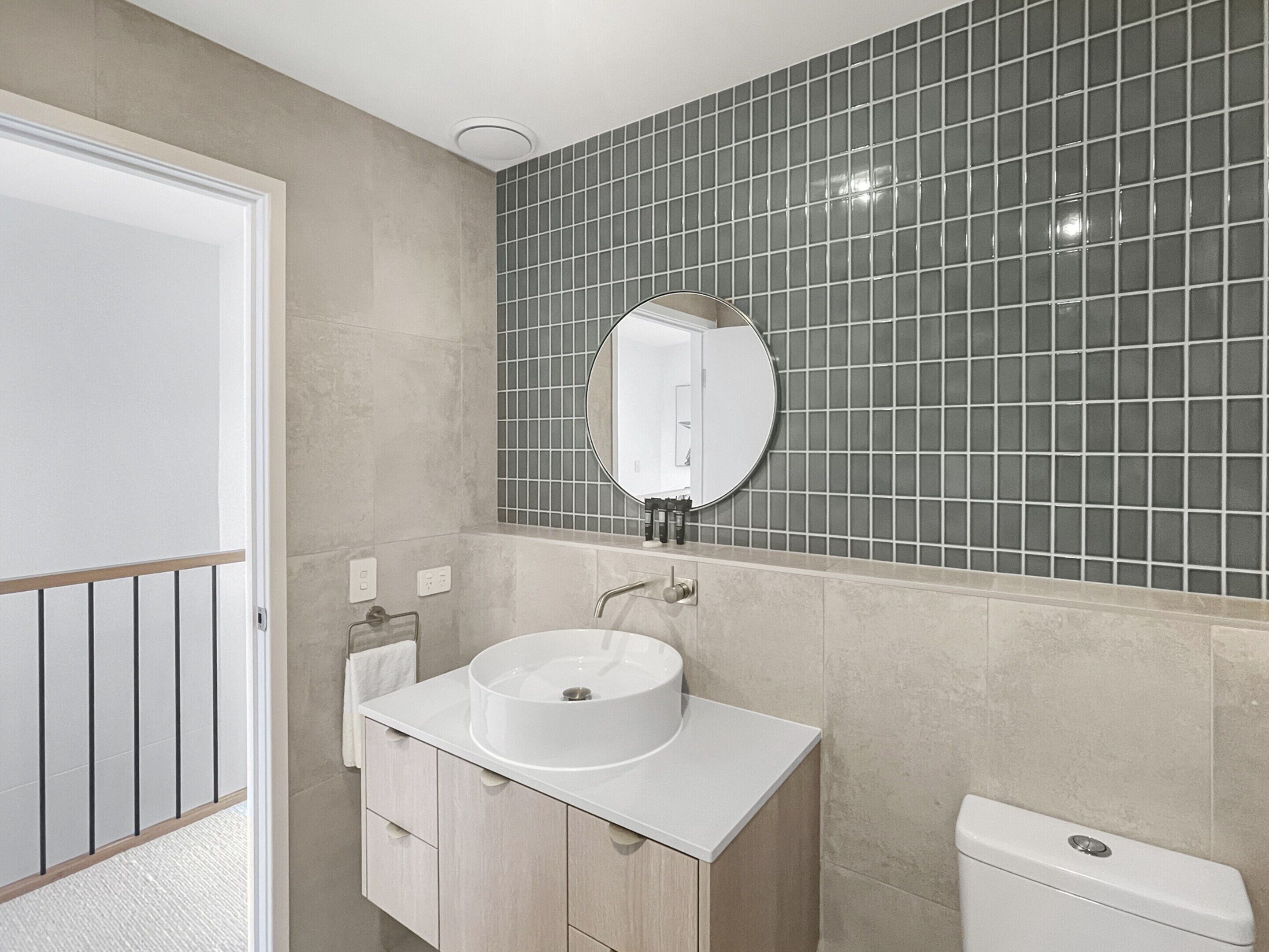A bathroom with a white sink, a round mirror, and a toilet.