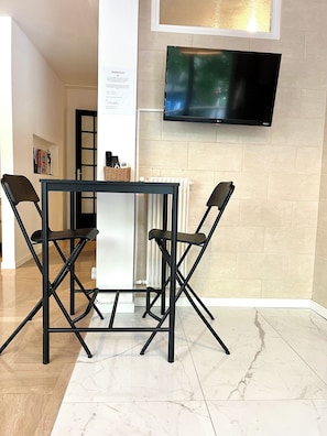 Una sala de estar moderna con una mesa de estructura metálica negra y dos sillas, un televisor de pantalla plana montado en la pared y un radiador blanco.