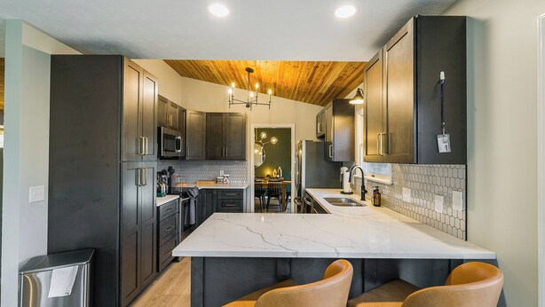 Una cocina moderna con armarios oscuros, una isla de mármol y techo de madera.