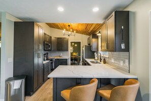 Une cuisine moderne avec des meubles de couleur sombre, un îlot en marbre et un plafond en bois.