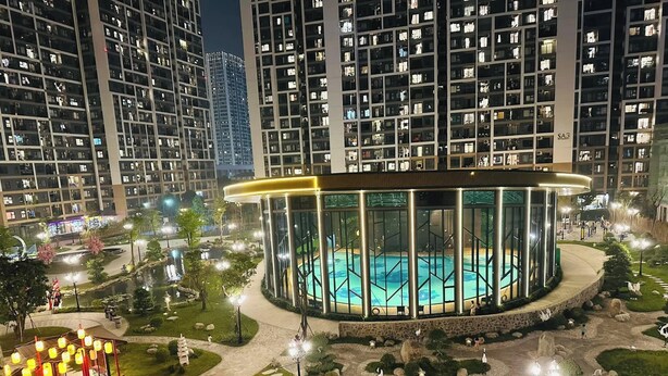 Un edificio moderno con una estructura circular de vidrio que rodea una piscina, todo ello rodeado de jardines ajardinados y senderos.