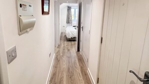 Een smalle gang met houten vloeren, witte muren en een bed in de verte.