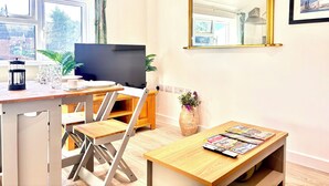 Een moderne woonkamer met een televisie, een koffiezetapparaat en een eethoek met een tafel en stoelen.
