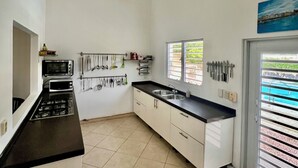 A kitchen with a gas stove, microwave, and sink. There is a ceiling fan, a window with blinds, and a door leading outside. - ~Nos Yemaya~ 2BR+Pool ~ Walking distance to playa Lagun! (Lagun)