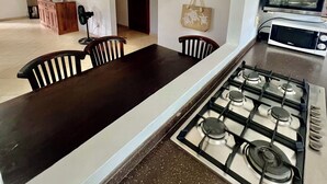 A modern kitchen with a gas stove, a microwave, and a dining area with a long table and chairs. - ~Nos Yemaya~ 2BR+Pool ~ Walking distance to playa Lagun! (Lagun)