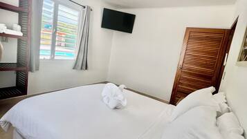 A hotel room with a bed, a flat-screen TV mounted on the wall, a wooden door, and a window with curtains.