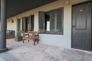 Entrada de un edificio con un área empedrada de piedra, un banco de madera, una planta en maceta y una puerta con el número 28.