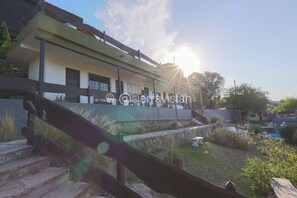 Un edificio moderno con techo plano, una escalera que lleva a un balcón y un jardín bien cuidado.