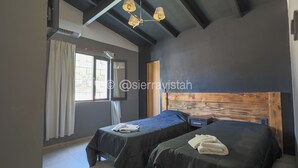 Habitación de hotel con dos camas, cabecero de madera, ventilador de techo y ventana con cortinas.