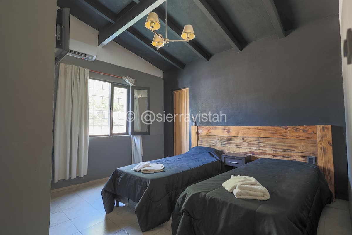 A hotel room with two beds, a wooden headboard, a ceiling fan, and a window with curtains.