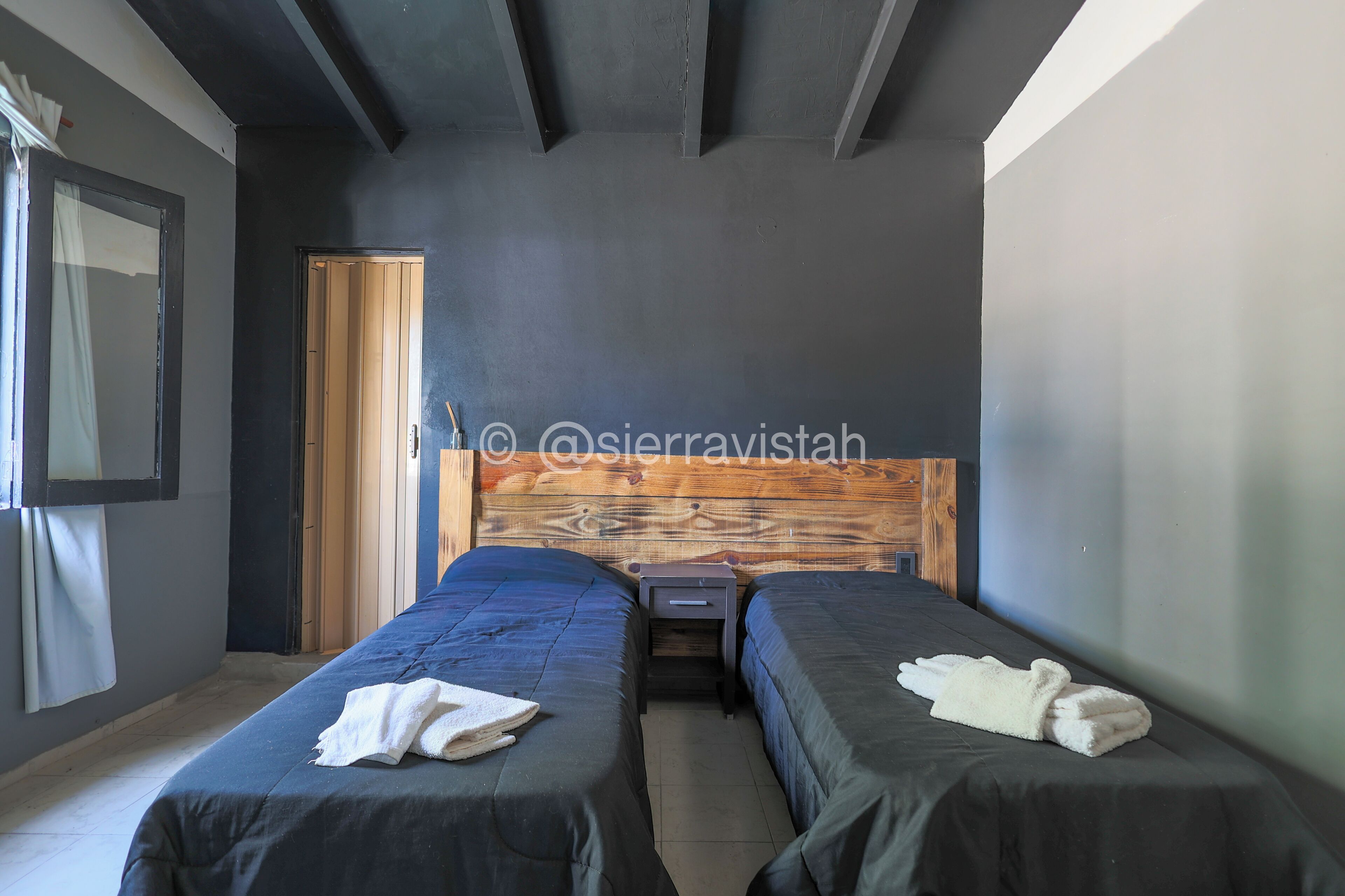 A bedroom with two beds, a wooden headboard, a nightstand, and a door.