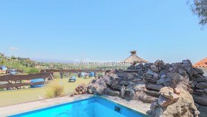 Una piscina con vistas al campo, una valla de madera y una estructura de techo de paja.