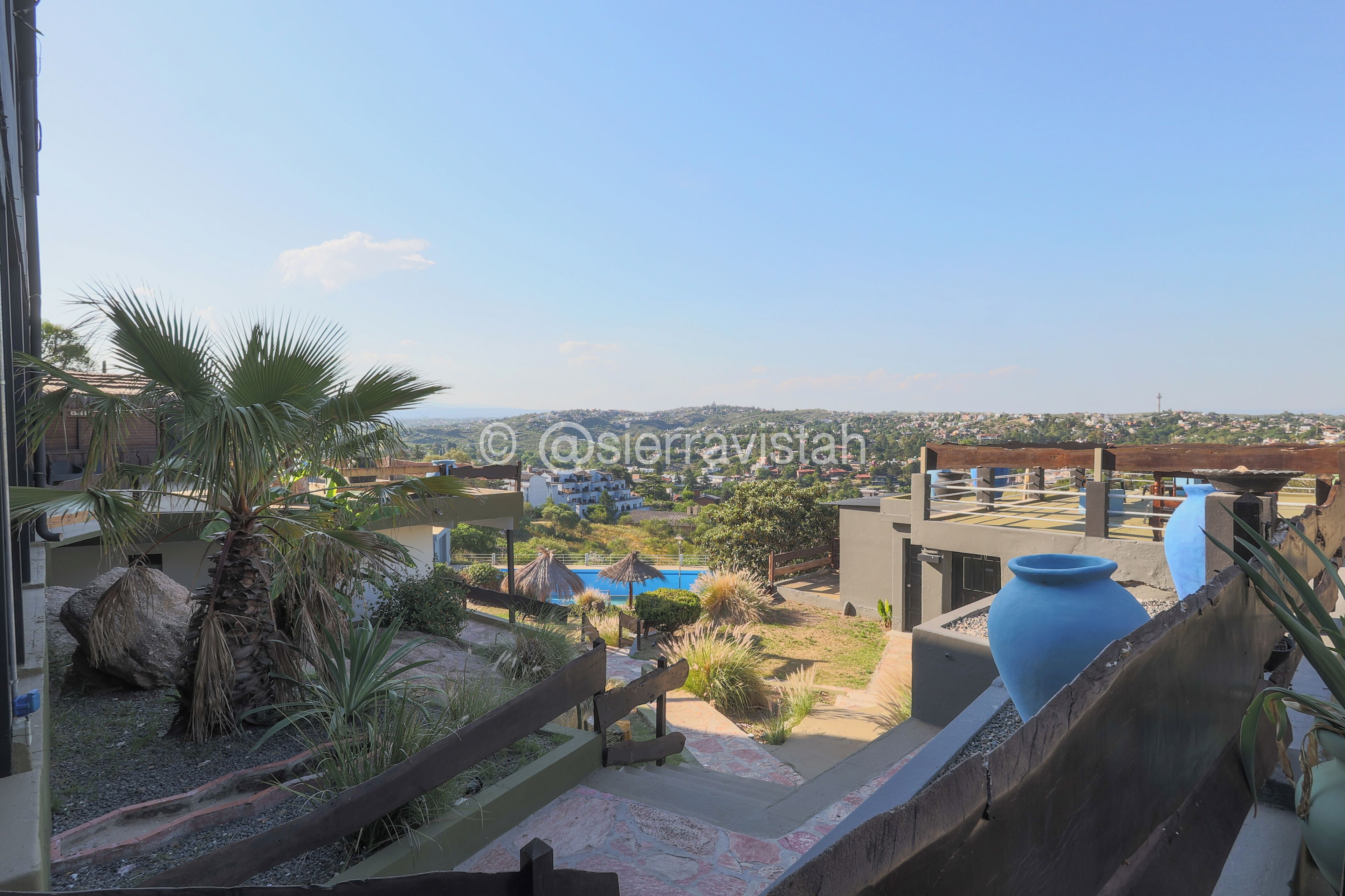Un jardín en la azotea con palmeras, una piscina y grandes jarrones.