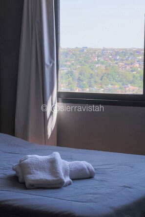 Un lit avec des serviettes blanches et une vue sur le paysage urbain par la fenêtre.