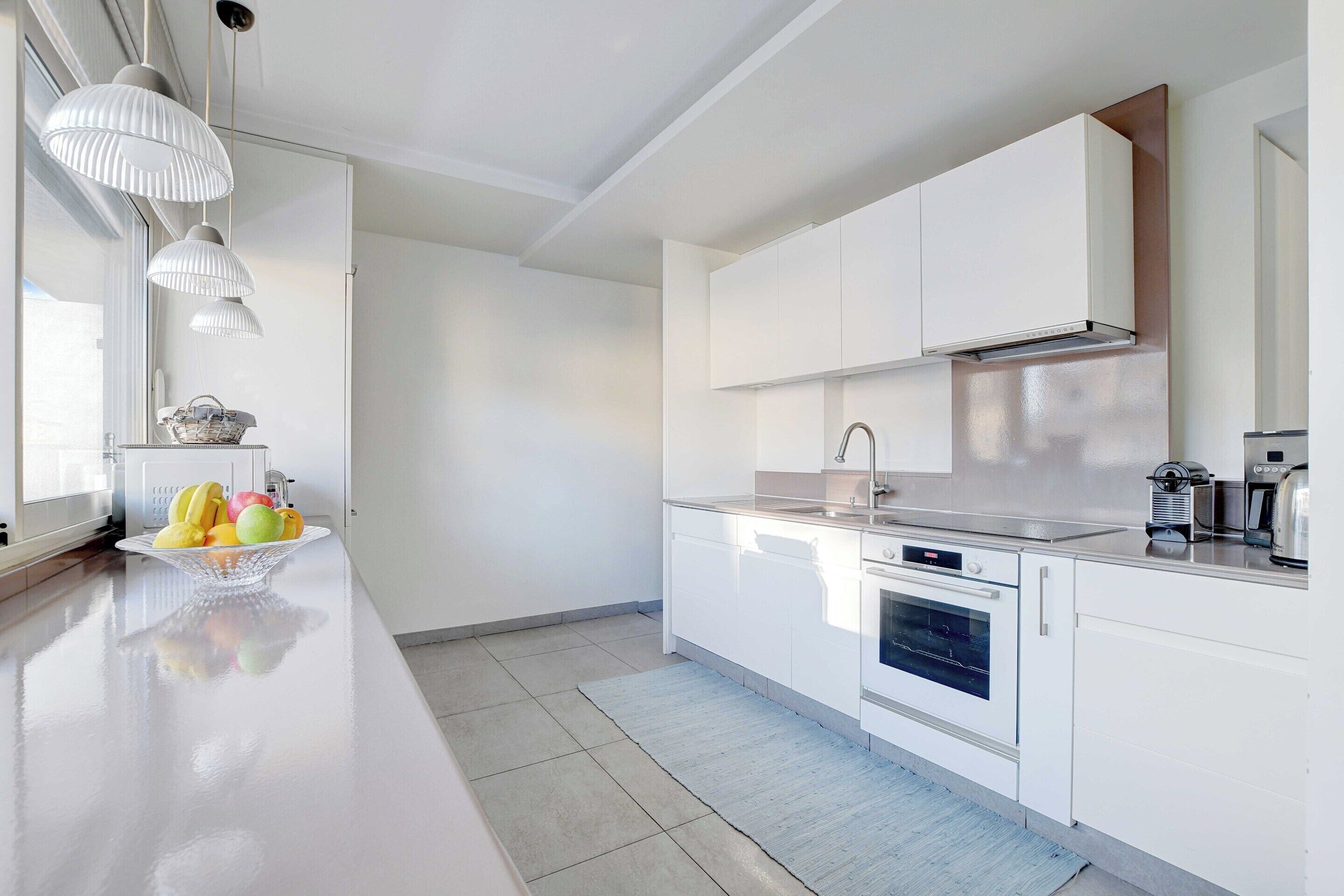 Una cocina moderna con armarios blancos, una campana extractora de acero inoxidable y una encimera con un frutero.