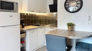 Une cuisine compacte avec des meubles blancs, un four à micro-ondes encastré, un lave-vaisselle et un petit coin repas comprenant deux chaises et une table ronde.