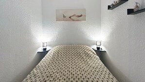 Une chambre à coucher comprenant un lit, deux lampes de chevet, une étagère fixée au mur avec des objets décoratifs, et un tableau encadré au-dessus du lit.