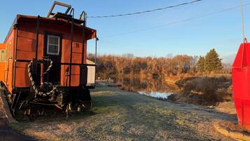 A train car with a ladder and a rope, parked beside a road with a grassy area and trees in the background.