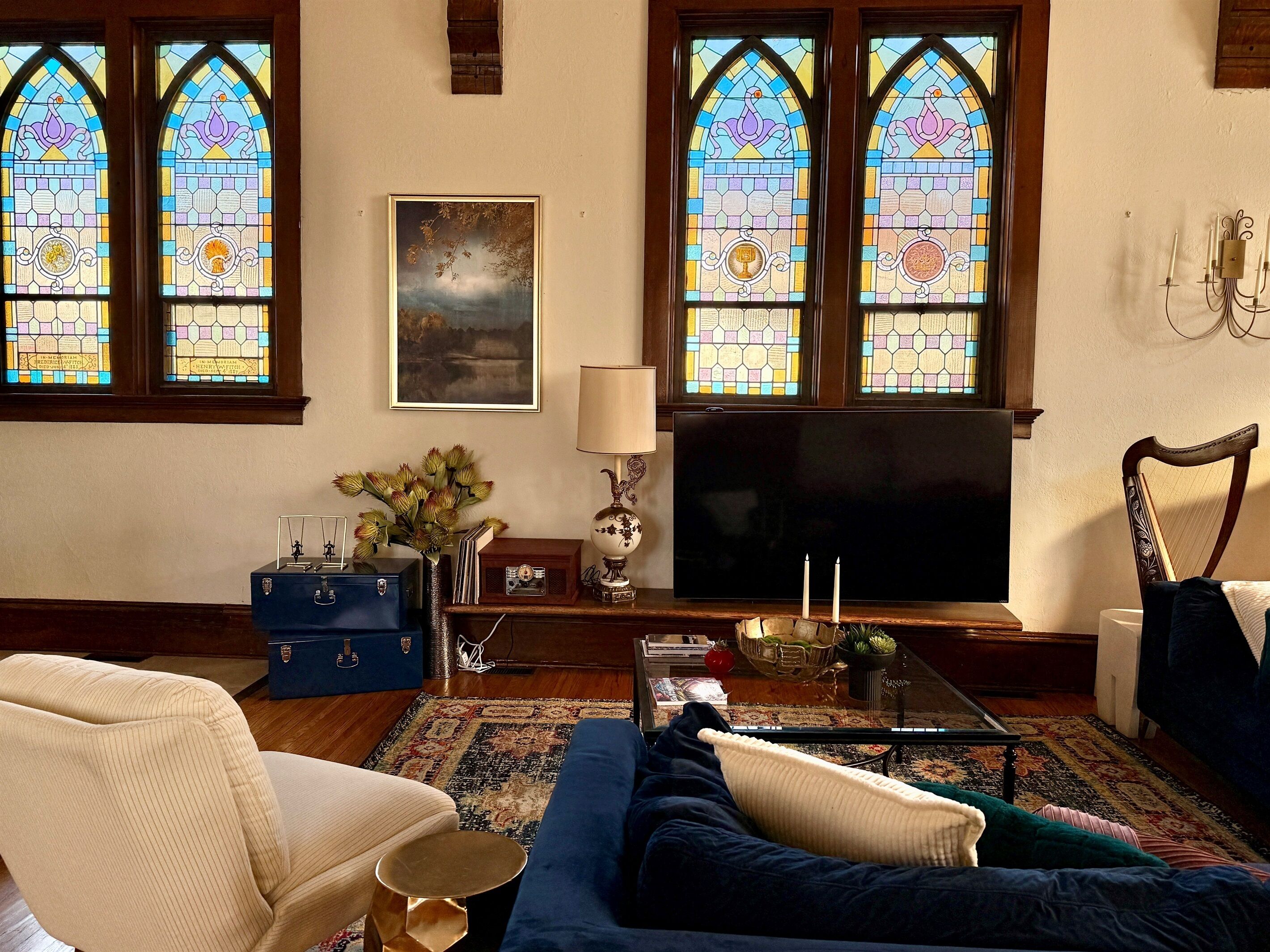 A living room with a large flat-screen TV, two stained glass windows, a sofa, a coffee table, and a decorative lamp.