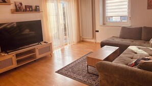 A living room with a flat-screen TV, a sofa, a coffee table, and a patterned rug.