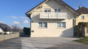 A two-story residential building with a balcony, a driveway, and a clear sky.