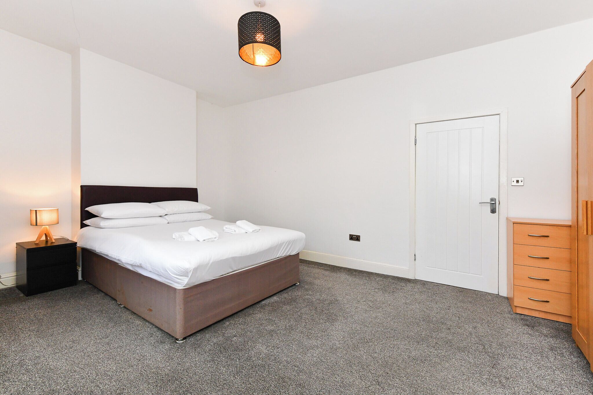 Ein Schlafzimmer mit Bett, Nachttisch, Kleiderschrank und einer Tür.